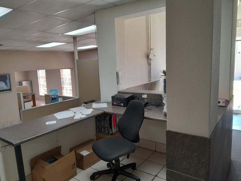 A functional office reception area featuring a built-in desk, tiled flooring, and a drop ceiling, providing a practical workspace for business operations.