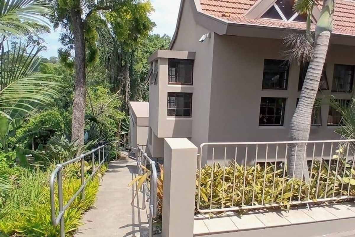 Rear exterior view of the property featuring a concrete pathway, metal security railings, and established garden surroundings.
