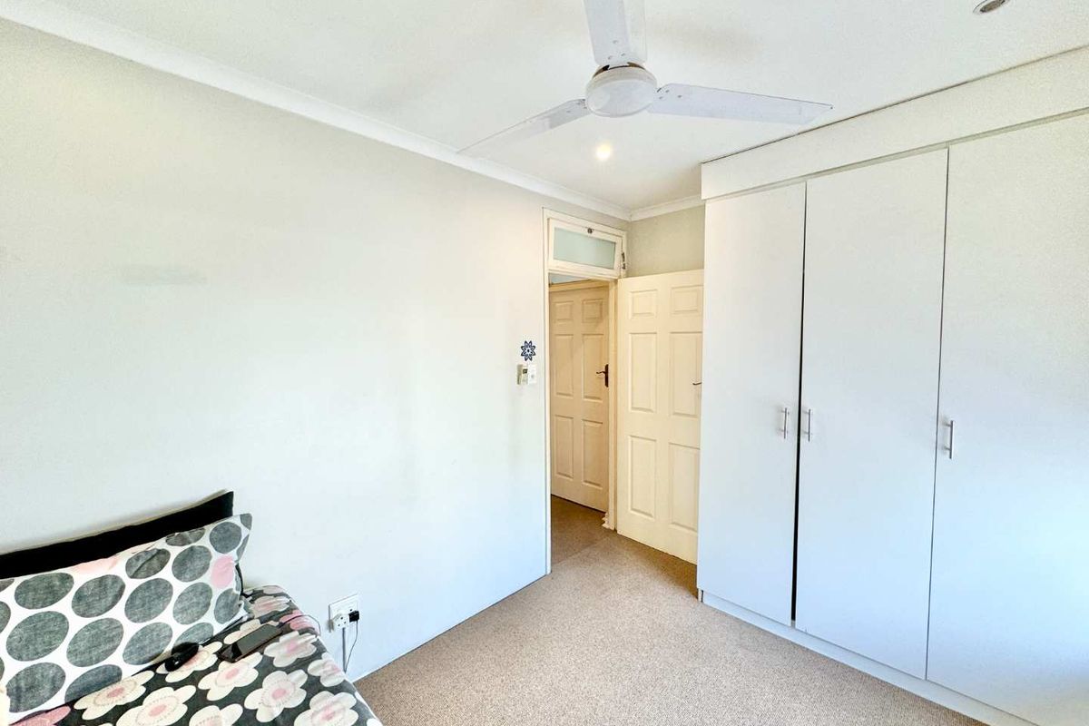 A functional bedroom featuring built-in cupboards, carpeted flooring, and a ceiling fan, offering a clean and neutral space.