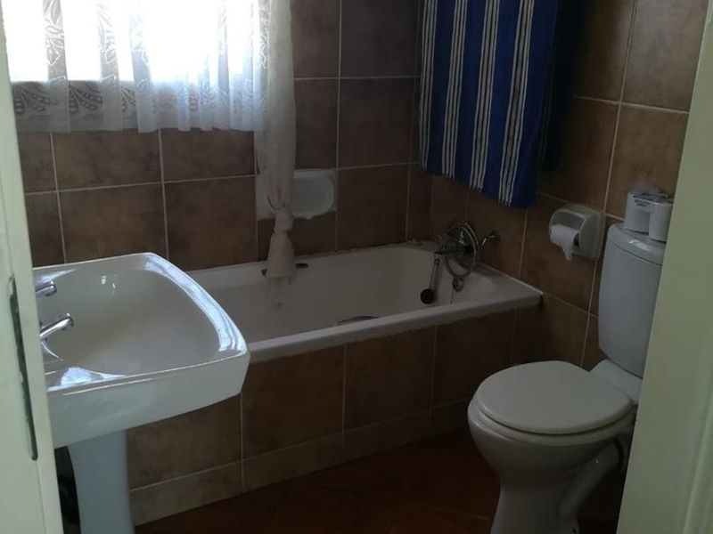 A functional bathroom featuring a pedestal basin, a built-in bathtub with tiled surround, and a standard toilet with tiled flooring and wall finishes.