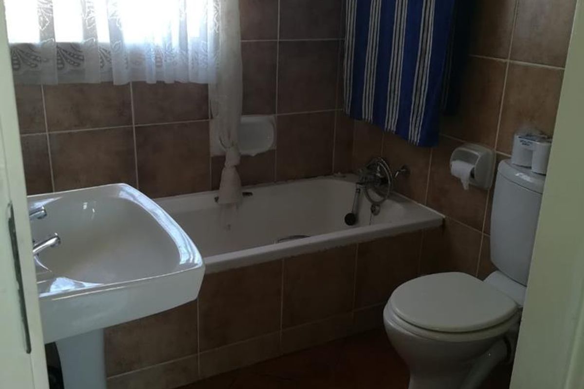 A functional bathroom featuring a pedestal basin, a built-in bathtub with tiled surround, and a standard toilet with tiled flooring and wall finishes.