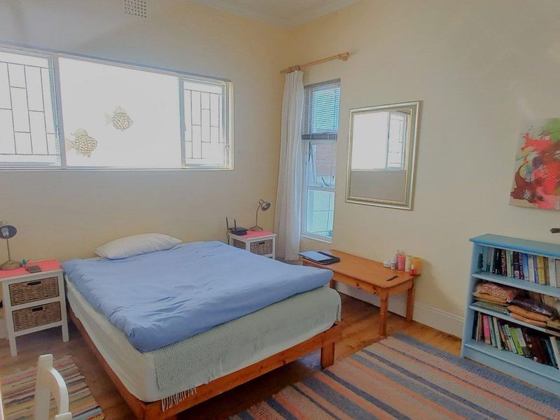 A well-lit bedroom featuring timber flooring, large windows with security bars, and neutral wall finishes.