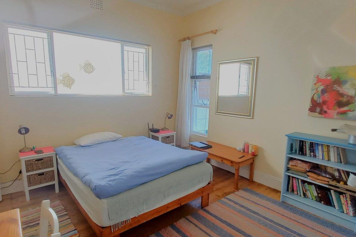 A well-lit bedroom featuring timber flooring, large windows with security bars, and neutral wall finishes.