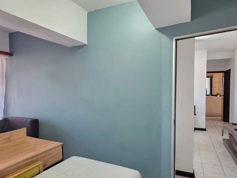 A bedroom featuring tiled flooring and a security gate on the window, with a view of the exterior and access to the hallway.