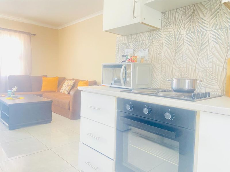 Open-plan living area featuring a compact kitchen with built-in oven, hob, extractor fan, and decorative tiled backsplash, flowing into the adjacent lounge space.