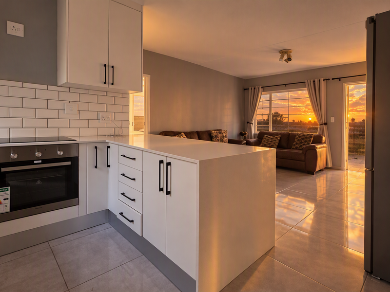 Modern open-plan kitchen and living area featuring sleek white cabinetry, subway tile backsplash, and polished tiled flooring with sunset views.