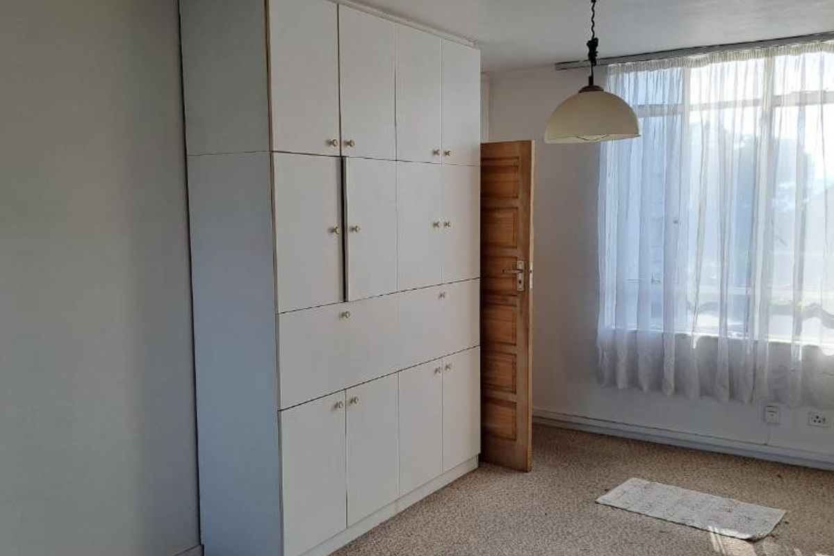 A bedroom featuring built-in cupboards, carpeted flooring, and a pendant light fixture. The room is vacant and ready for renovation.