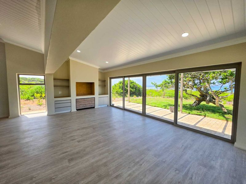 Spacious, light-filled living area featuring modern laminate flooring, recessed lighting, built-in cabinetry, and large sliding glass doors opening to a garden view.