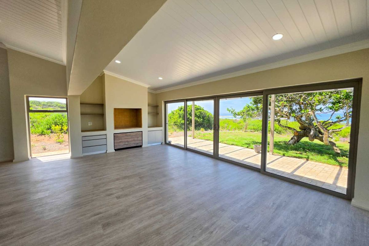 Spacious, light-filled living area featuring modern laminate flooring, recessed lighting, built-in cabinetry, and large sliding glass doors opening to a garden view.