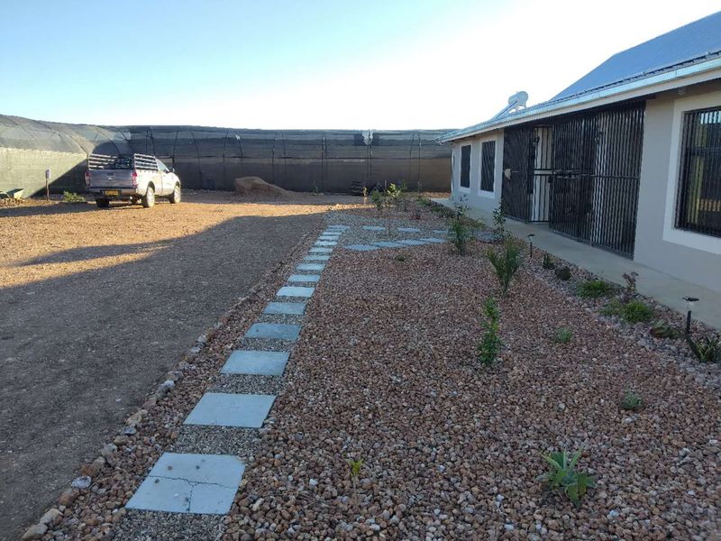 Rear exterior view of the property featuring gravel landscaping, stone pathway, and security bars on windows, with a large shade cloth enclosure in the background.