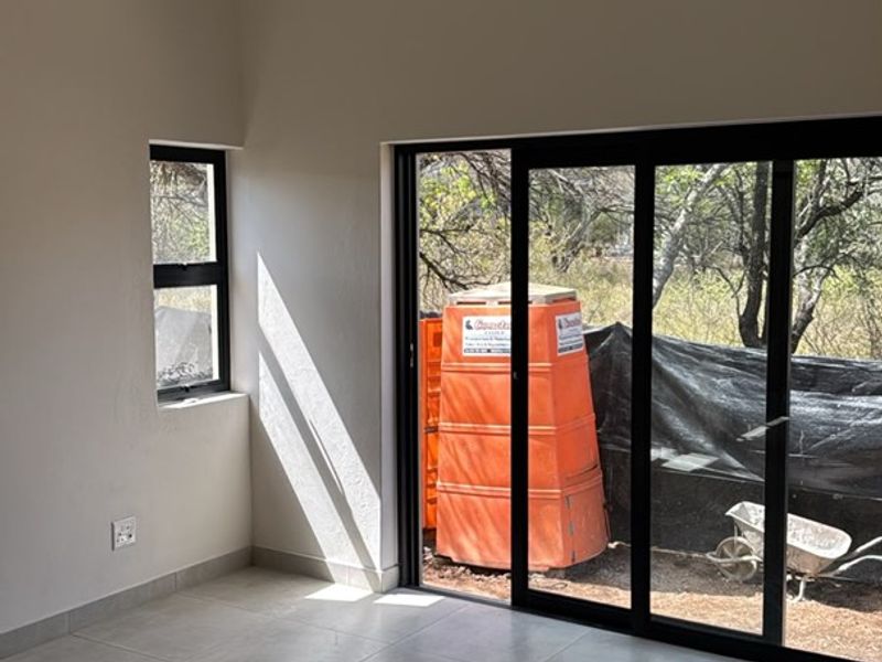 A bright, empty living area featuring modern tiled flooring, a tongue and groove ceiling, and large sliding glass doors leading to the exterior.