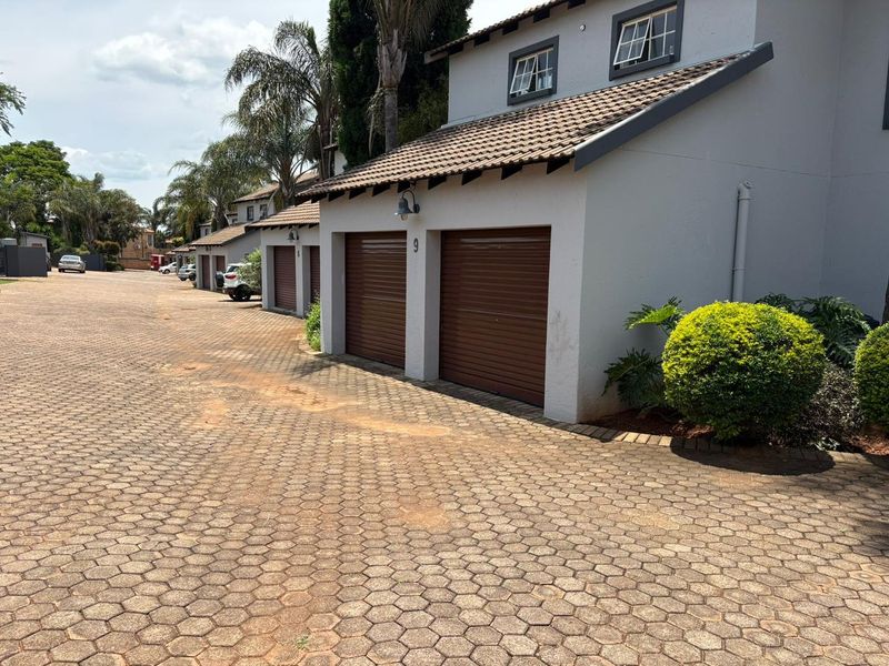 Front view of a cluster property featuring multiple garage units with brown roller doors and a paved driveway in a residential complex.