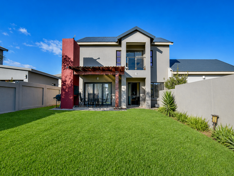 Rear view of a modern double-story house featuring a manicured lawn, a timber pergola, and a built-in braai area.