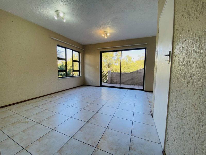 An empty living room featuring tiled flooring, textured walls, and a sliding glass door providing access to an outdoor balcony area.