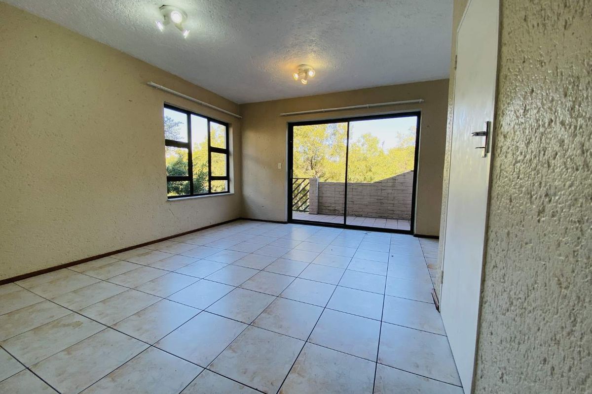An empty living room featuring tiled flooring, textured walls, and a sliding glass door providing access to an outdoor balcony area.