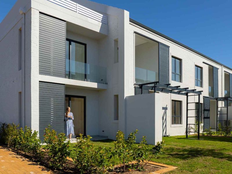 Modern apartment exterior featuring white brick facade, glass balustrades, and private ground floor patio area with pergola.