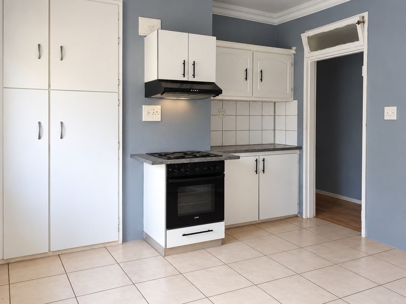 A clean, functional kitchen featuring white cabinetry, a built-in extractor fan, a freestanding stove, and neutral tiled flooring.