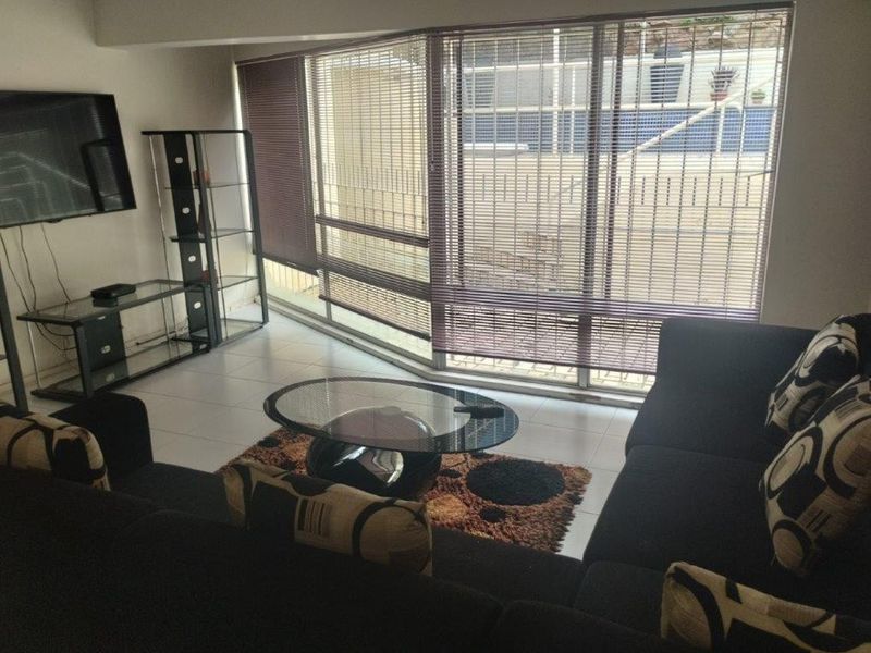 A living room featuring tiled flooring and large windows with venetian blinds, offering natural light and a view of the exterior.