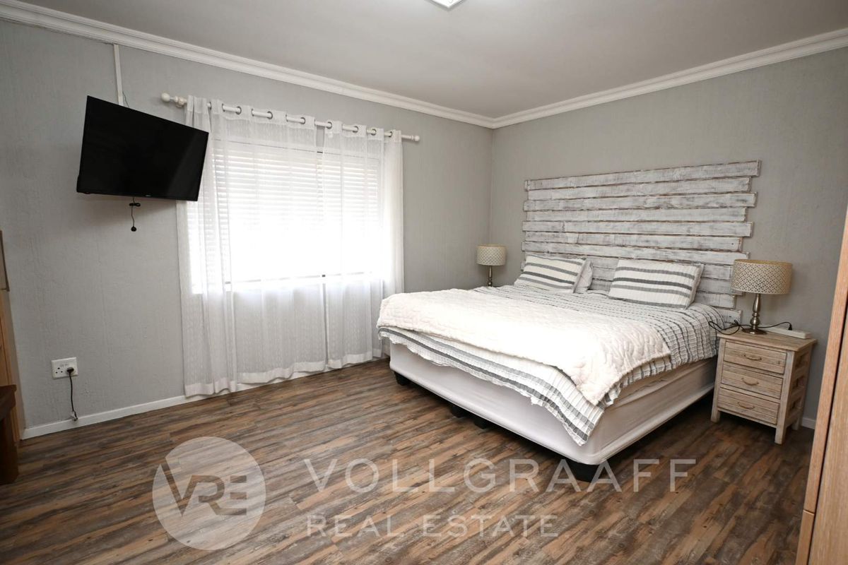 A well-maintained bedroom featuring wood-look laminate flooring, crown molding, and a neutral color palette.