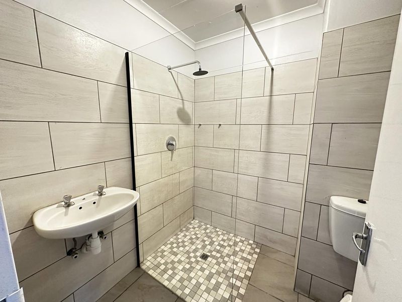 A modern, clean bathroom featuring a walk-in shower with a glass screen, wall-mounted basin, and neutral tiled finishes throughout.