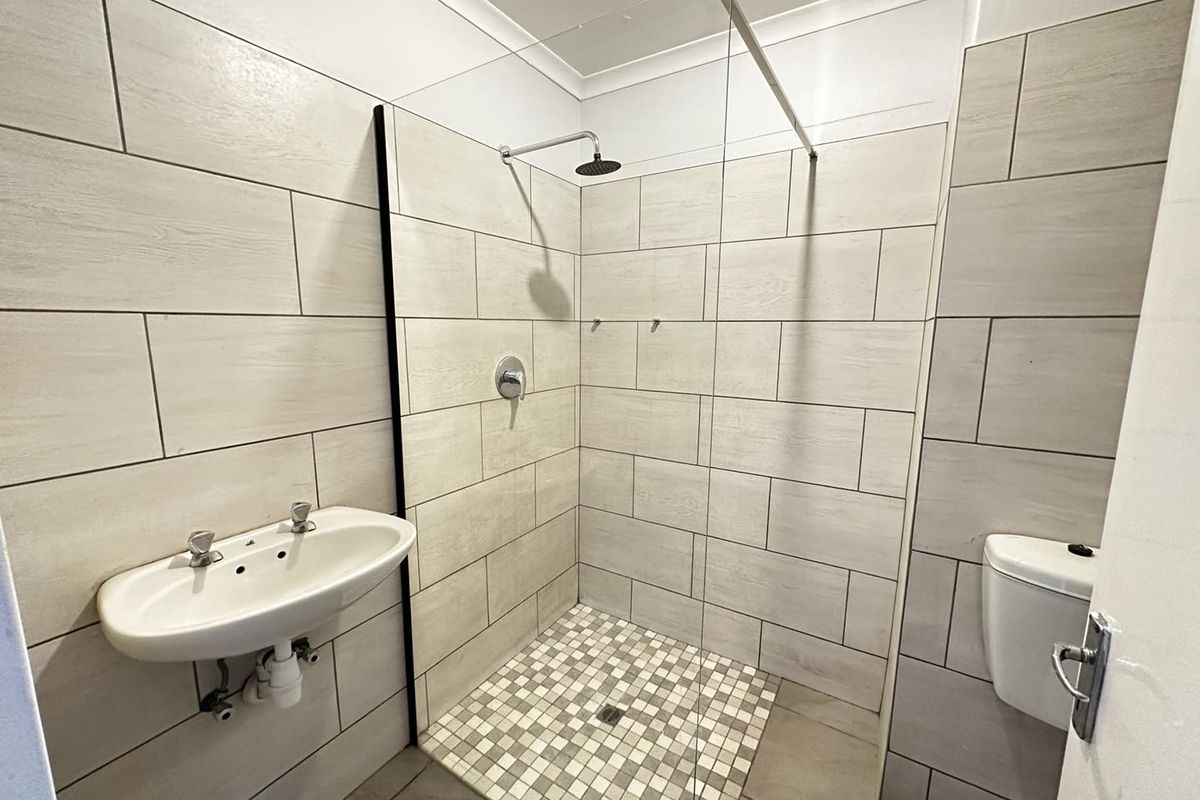 A modern, clean bathroom featuring a walk-in shower with a glass screen, wall-mounted basin, and neutral tiled finishes throughout.