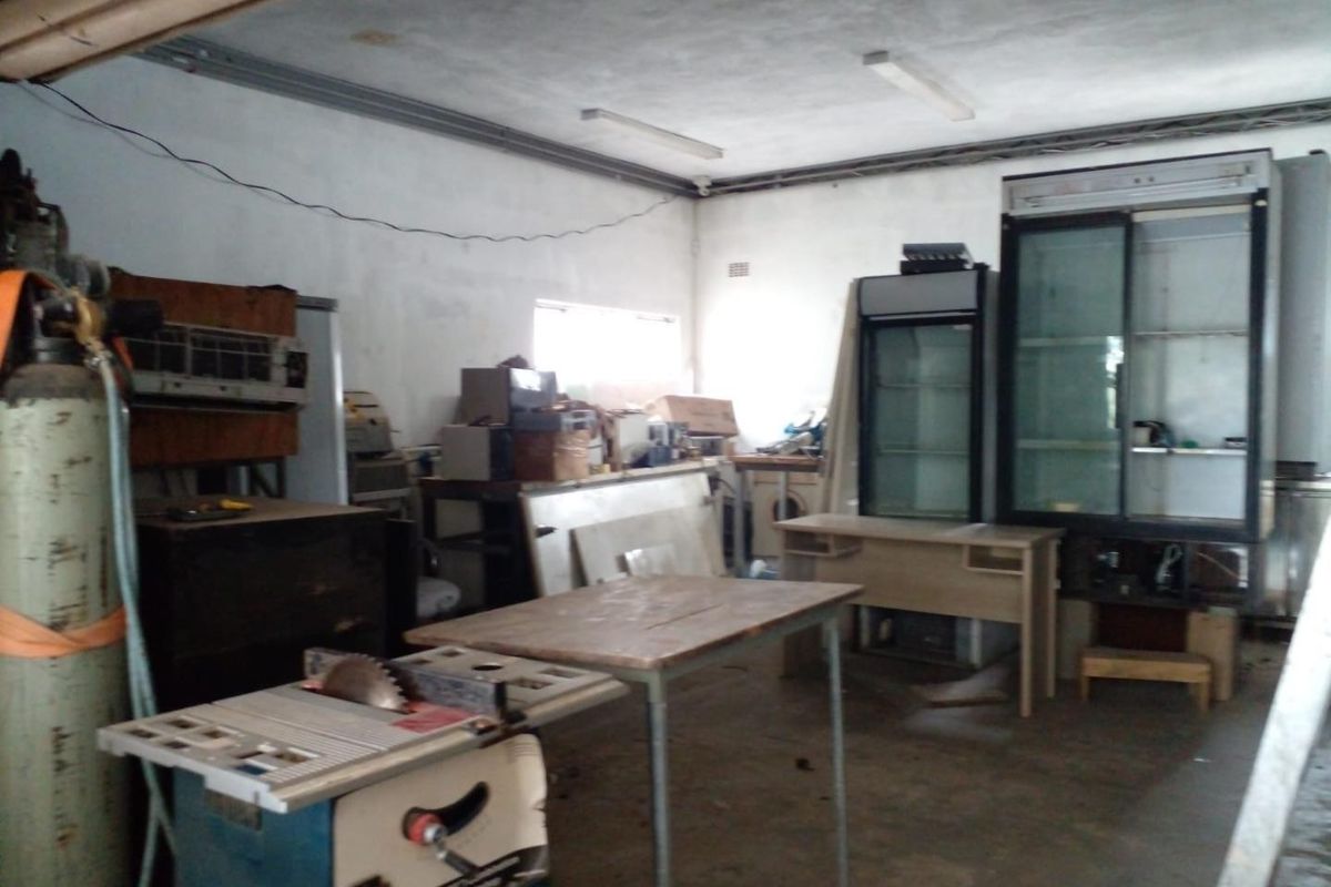 A utilitarian workspace featuring concrete flooring and overhead fluorescent lighting, currently used for storage and workshop activities.