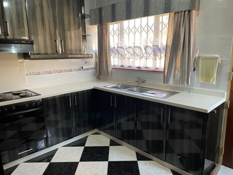 A functional kitchen featuring dark wood-grain cabinetry, white countertops, a double sink, and a built-in oven with an electric hob.