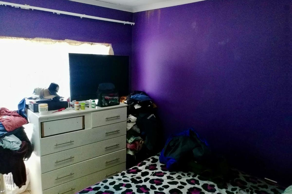 A bedroom featuring purple painted walls and a window with a curtain rod.