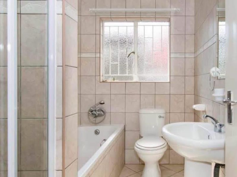 A functional bathroom featuring a shower enclosure, bathtub, pedestal sink, and toilet, finished with neutral wall and floor tiling.