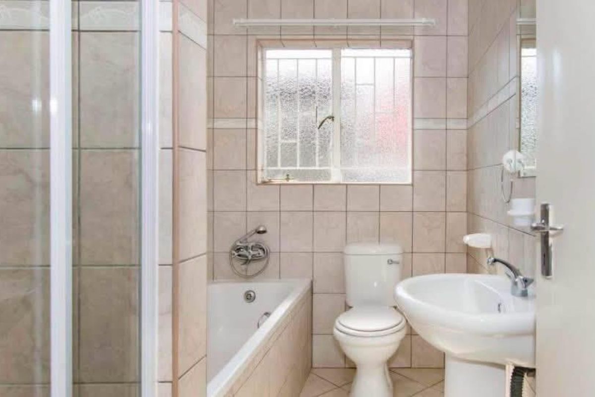 A functional bathroom featuring a shower enclosure, bathtub, pedestal sink, and toilet, finished with neutral wall and floor tiling.