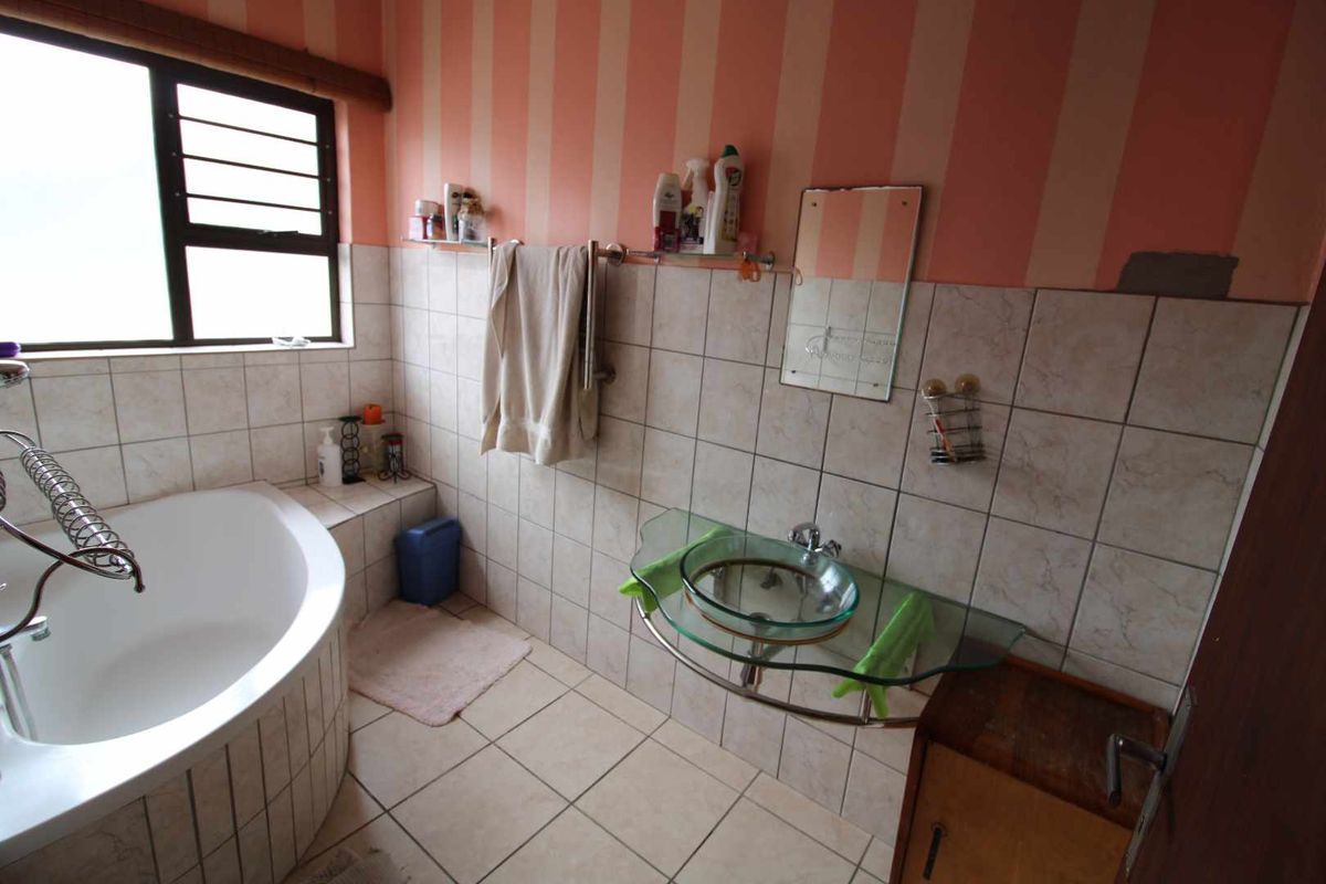 A bathroom featuring a corner bathtub, a glass vessel sink with a wall-mounted faucet, and tiled walls with striped wallpaper.