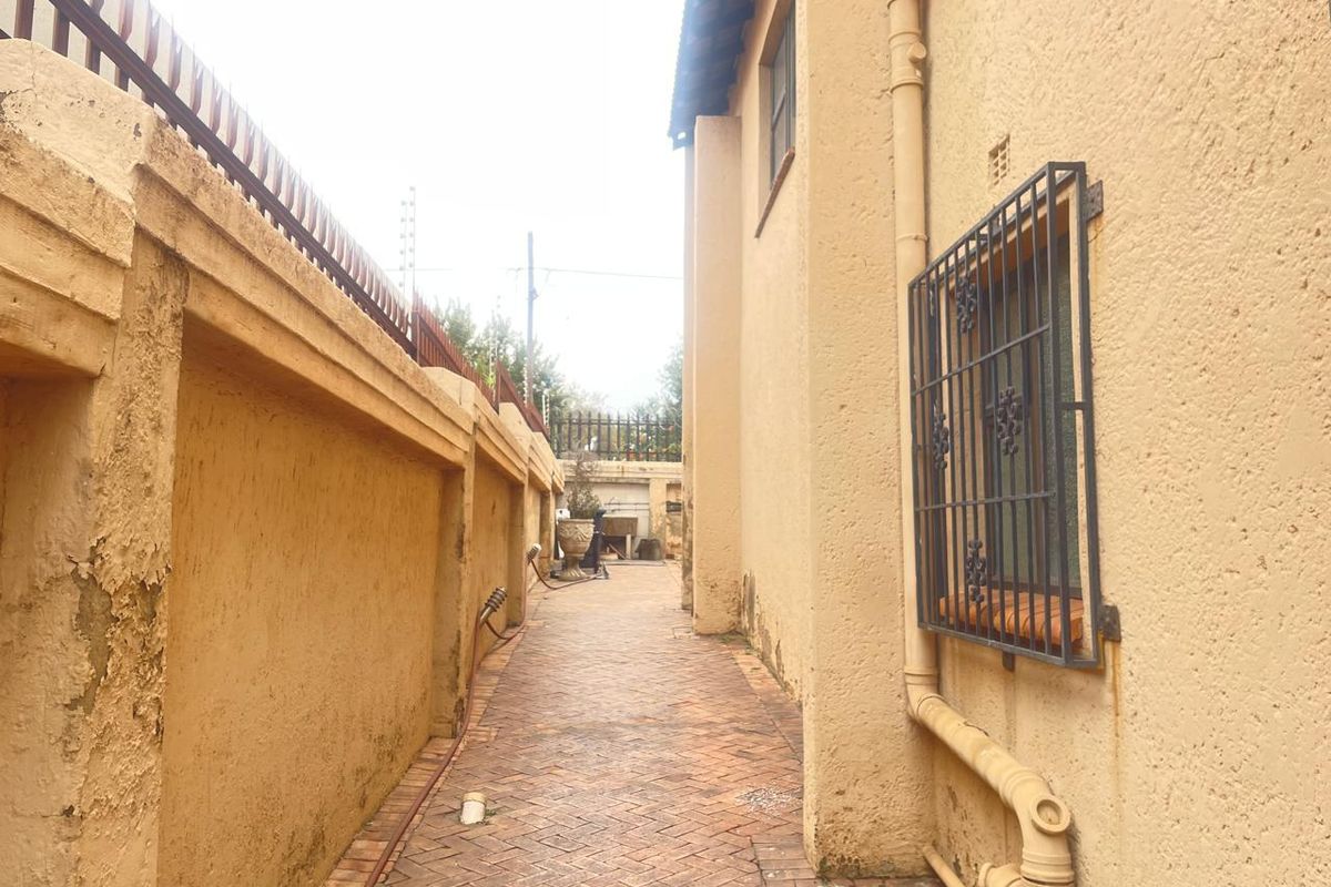 A narrow side passage of the house featuring brick paving, security bars on windows, and perimeter boundary walls.