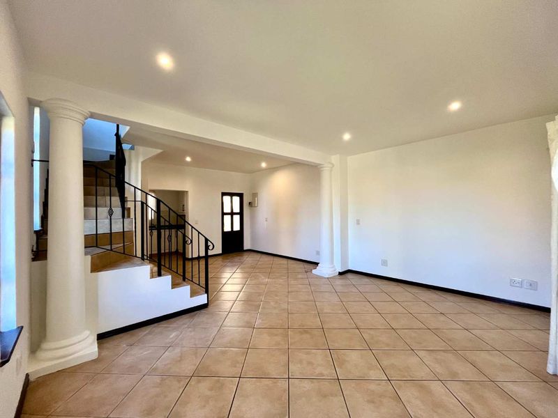 Spacious open-plan living area featuring neutral tiled flooring, decorative columns, and a staircase with wrought iron railing, offering a bright and versatile layout.