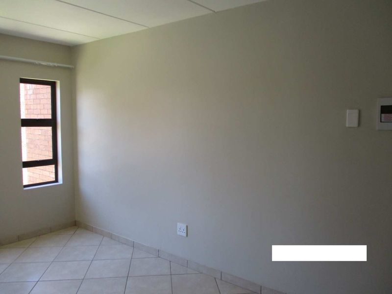 A clean, empty bedroom featuring neutral wall finishes, tiled flooring, and a single window providing natural light.
