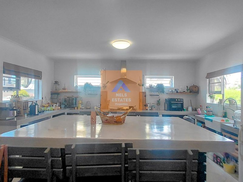 Spacious kitchen featuring a large central concrete island, built-in concrete countertops, an apron sink, and integrated shelving, offering a functional and rustic aesthetic.
