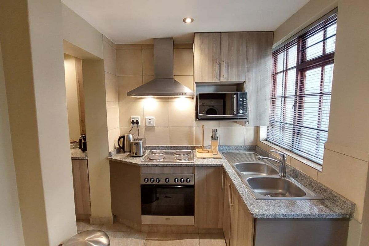Compact, functional kitchen featuring modern wood-finish cabinetry, granite countertops, stainless steel appliances, and a tiled backsplash with integrated lighting.
