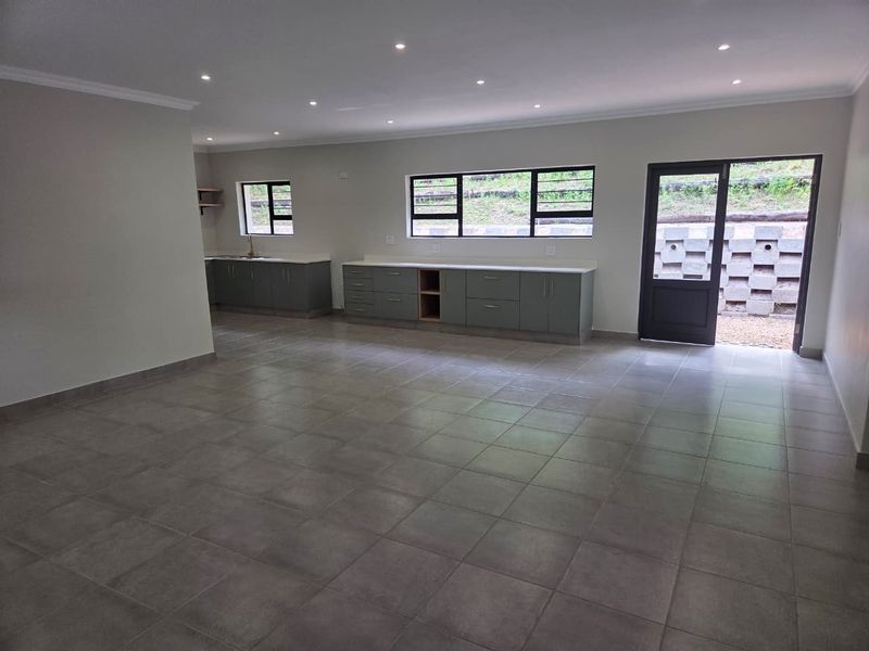Spacious open-plan living area featuring neutral tiled flooring, recessed lighting, and a modern kitchen area with built-in cabinetry and direct outdoor access.