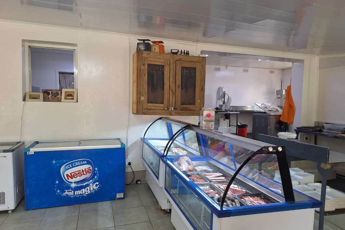 A functional commercial kitchen or butchery preparation area featuring tiled flooring, built-in cabinetry, and refrigerated display counters.