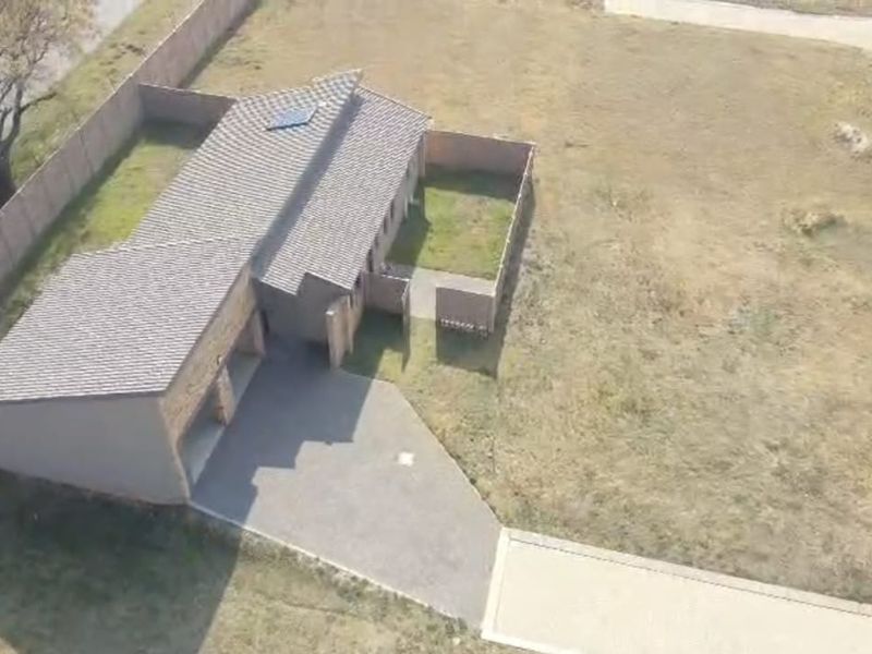 Aerial view of a residential property featuring a paved driveway, garage, and perimeter wall on a spacious plot.