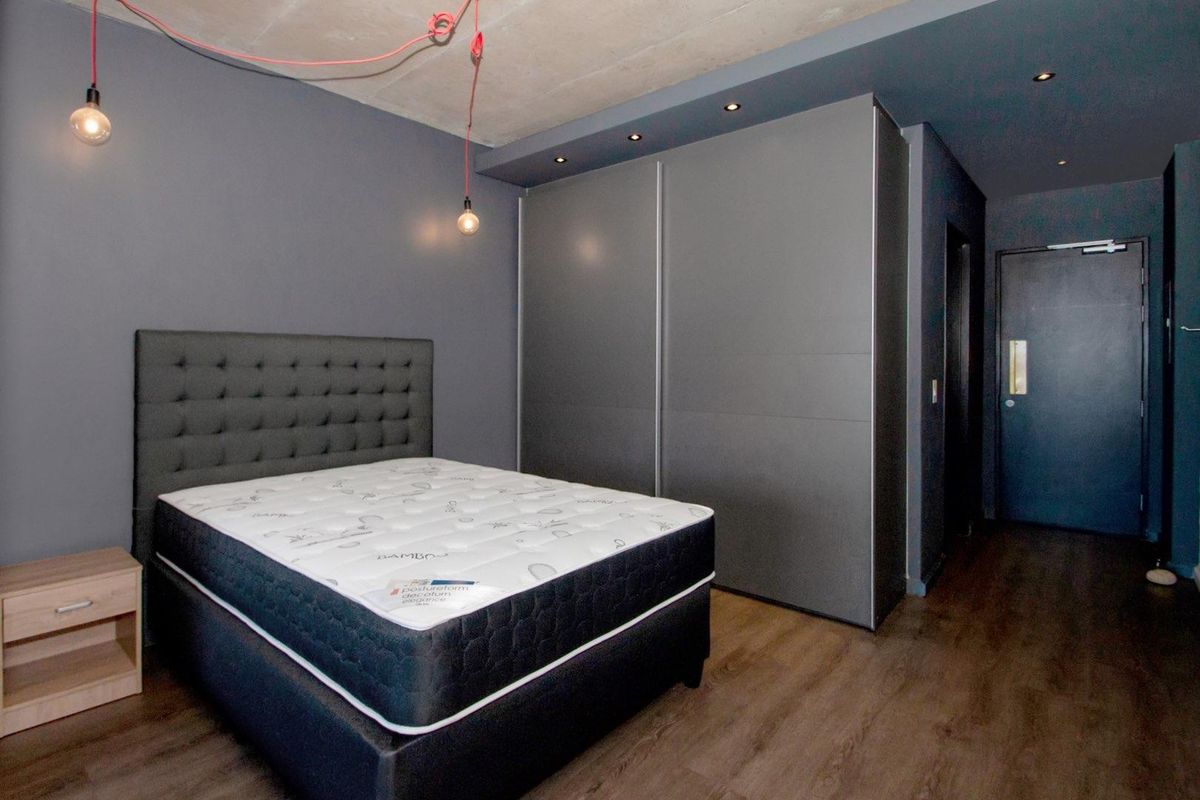 Modern bedroom featuring dark grey walls, exposed concrete ceiling, built-in sliding door wardrobes, and wood-look flooring.