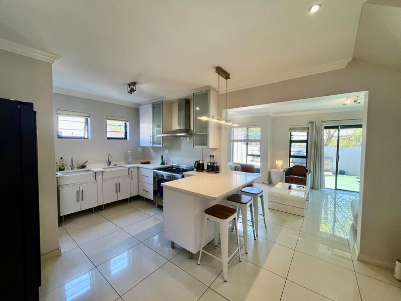 Modern open-plan kitchen and living area featuring a central island, quartz countertops, farmhouse sink, and seamless access to the outdoor patio through sliding doors.