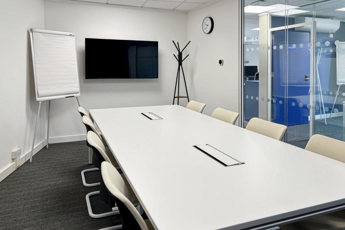 A modern, well-maintained office meeting room featuring a large conference table, glass partition walls, and professional recessed lighting.