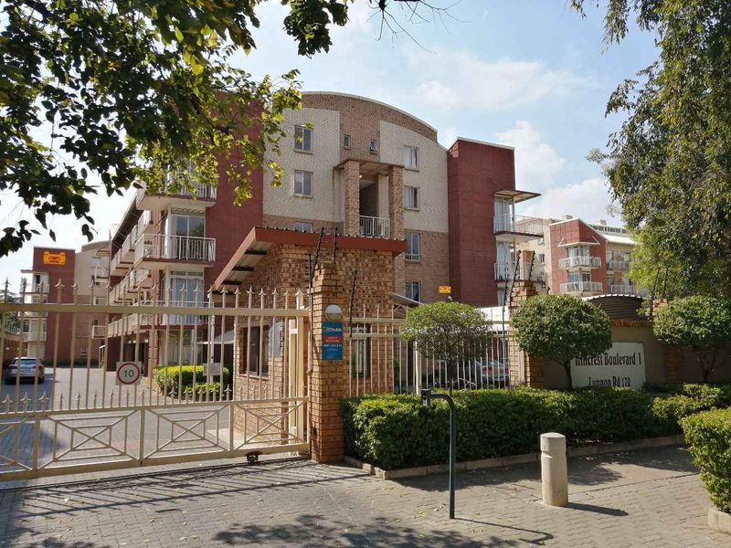 Front view of Pinecrest Boulevard I apartment complex featuring a secure gated entrance, brick facade, and multiple balconies.