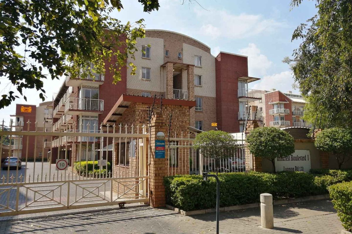 Front view of Pinecrest Boulevard I apartment complex featuring a secure gated entrance, brick facade, and multiple balconies.
