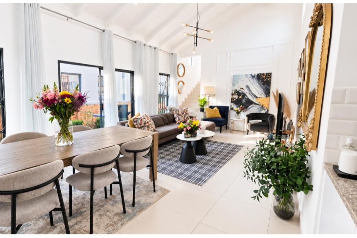 Spacious open-plan living and dining area featuring high vaulted ceilings with exposed beams, large sliding doors, and bright, modern tiled flooring.