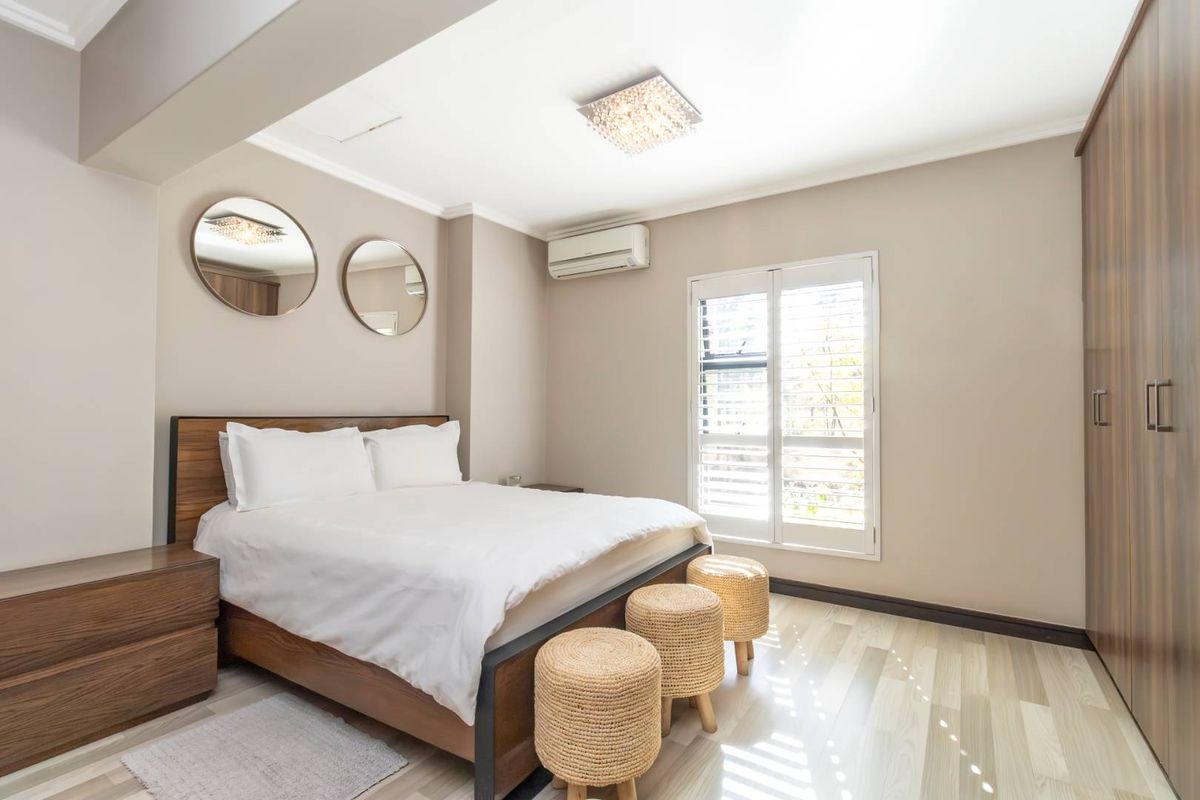 A well-maintained bedroom featuring laminate flooring, built-in cupboards, plantation shutters, and an integrated air conditioning unit.