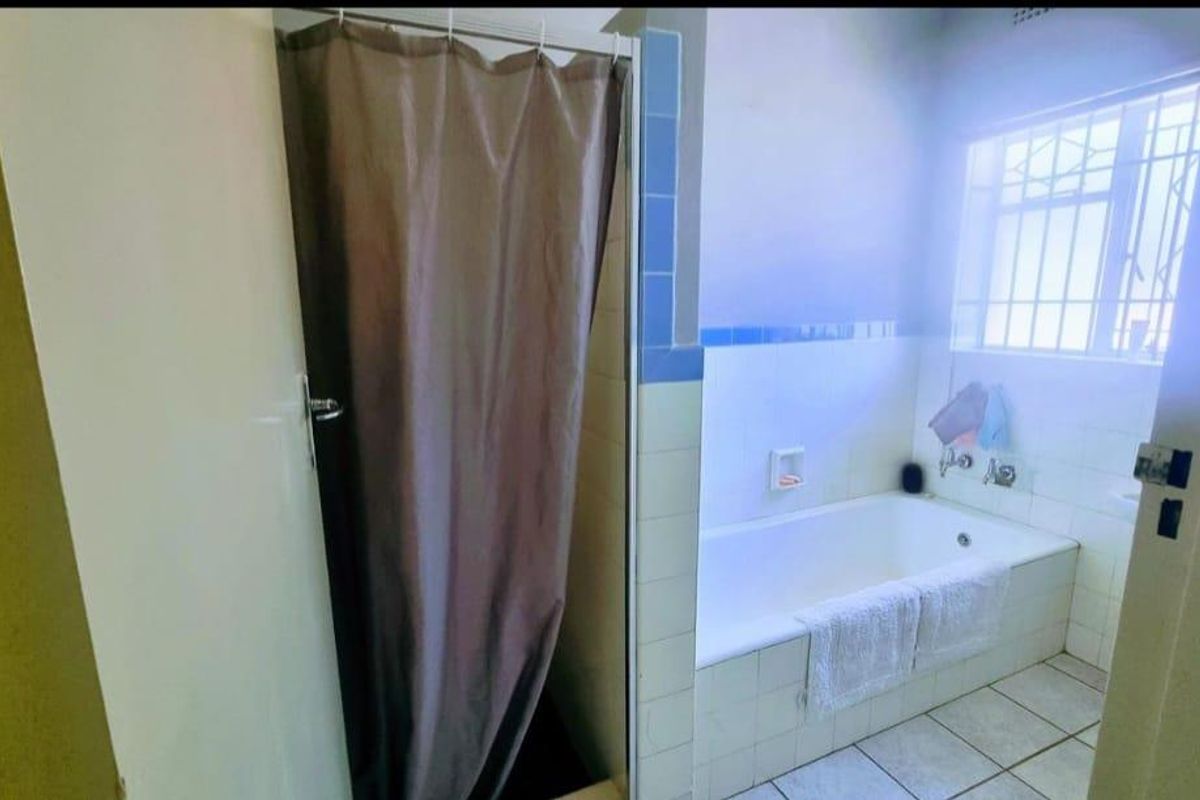 A functional bathroom featuring a built-in bathtub, separate shower enclosure, and tiled finishes, offering a practical layout with natural light.