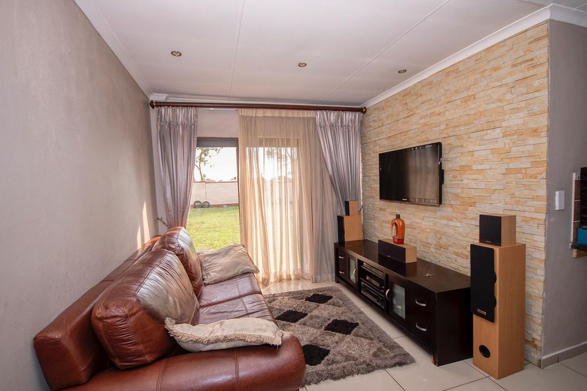 A comfortable living room featuring a textured stone accent wall, tiled flooring, and a sliding glass door providing access to the garden.