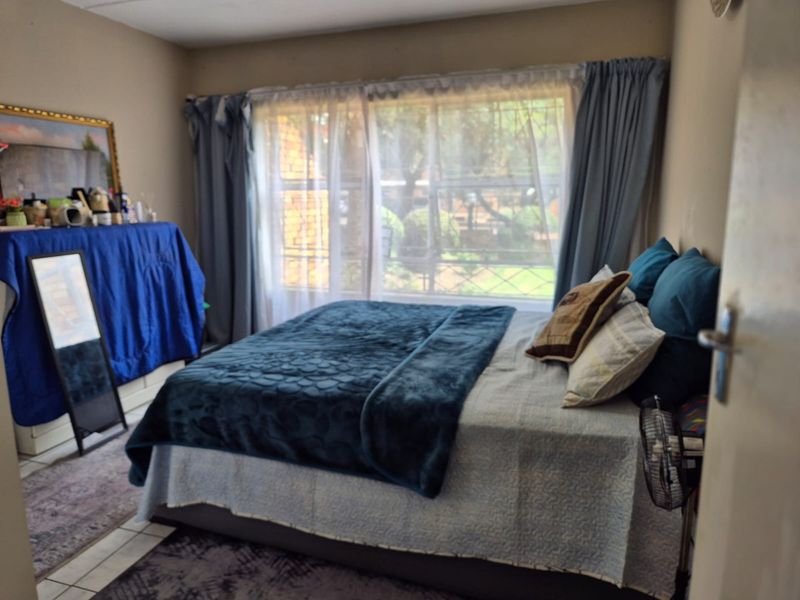 A bedroom featuring tiled flooring and a large window with curtain treatments, providing natural light to the space.