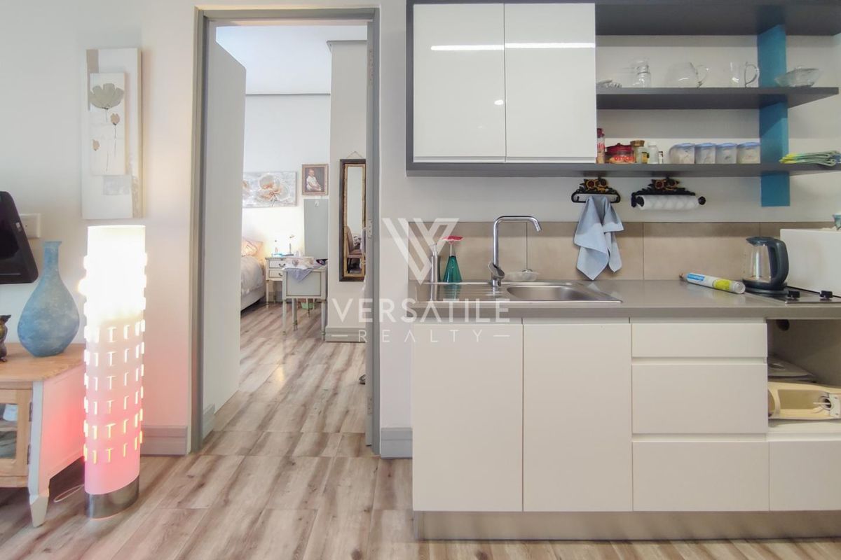 A compact, modern kitchen area featuring sleek white cabinetry, open shelving, and a stainless steel sink, seamlessly integrated into the living space.